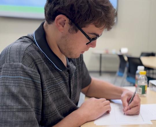 young man writing on a piece of paper in a conference room
